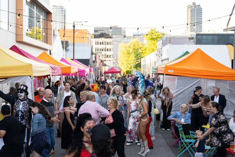 Crowded Gunson Street Party in Adelaide featuring colorful market stalls, string lights, costumed performers, and dancing crowds